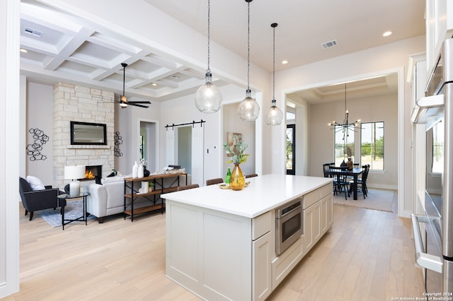 kitchen with a kitchen island, a barn door, white cabinets, beamed ceiling, and stainless steel microwave