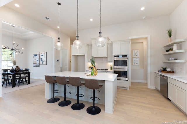 kitchen with light hardwood / wood-style floors, appliances with stainless steel finishes, backsplash, decorative light fixtures, and a center island