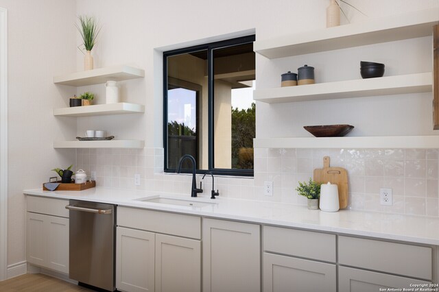 bar featuring tasteful backsplash, light stone countertops, sink, dishwasher, and light hardwood / wood-style flooring