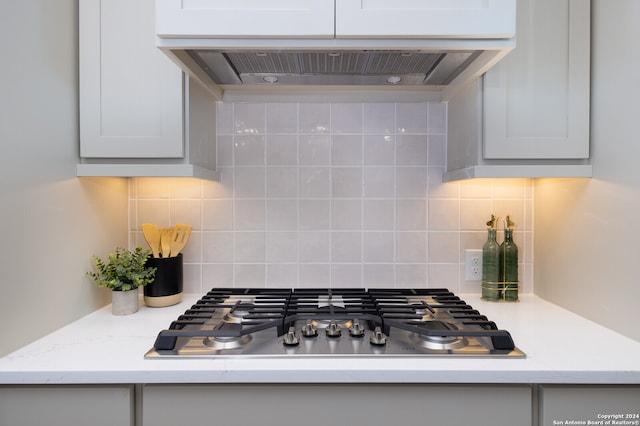 kitchen featuring stainless steel gas stovetop, extractor fan, light stone counters, and tasteful backsplash