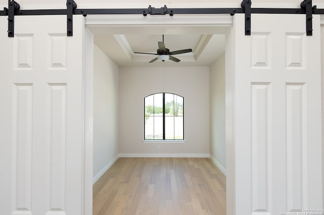 unfurnished room featuring a barn door, ceiling fan, light wood-type flooring, and a tray ceiling