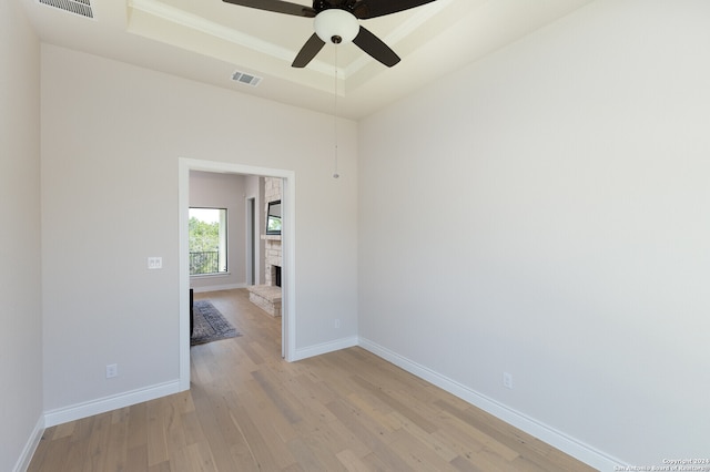 empty room with light wood-type flooring, a tray ceiling, and ceiling fan