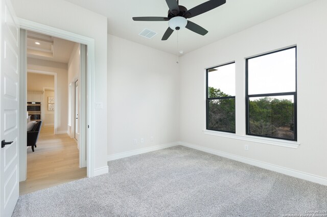 unfurnished room with light carpet, ceiling fan, and a tray ceiling