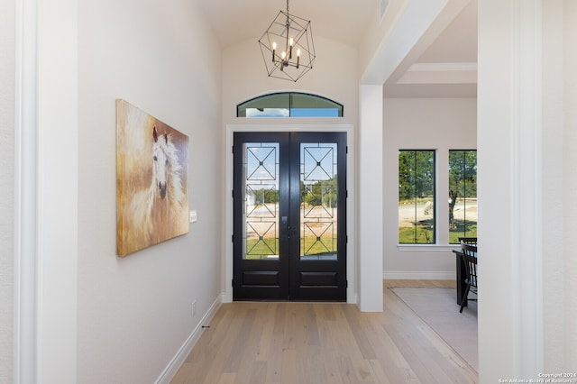 foyer entrance featuring french doors, light hardwood / wood-style floors, vaulted ceiling, and an inviting chandelier