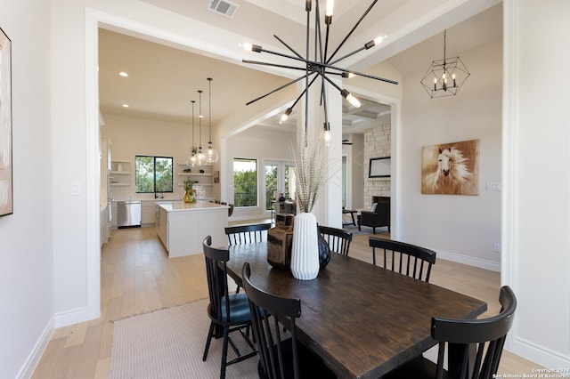 dining space featuring a stone fireplace, light hardwood / wood-style floors, and an inviting chandelier