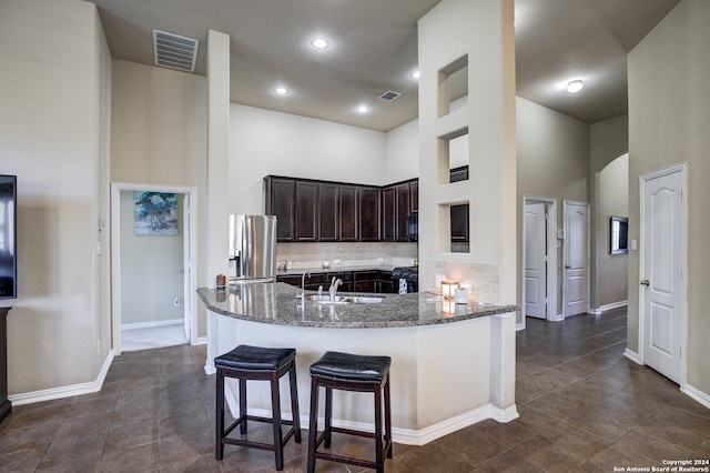 kitchen with appliances with stainless steel finishes, dark brown cabinetry, decorative backsplash, a high ceiling, and kitchen peninsula