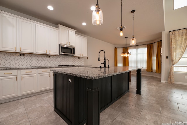 kitchen with white cabinetry, hanging light fixtures, and a center island with sink