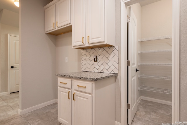 kitchen with white cabinetry, light tile patterned floors, light stone counters, and backsplash