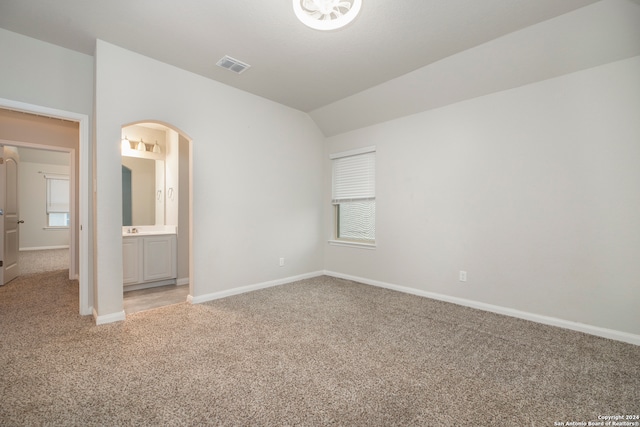 unfurnished bedroom with connected bathroom, vaulted ceiling, and light carpet