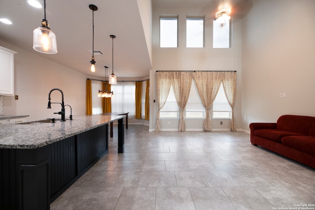 kitchen featuring white cabinetry, sink, light stone countertops, an inviting chandelier, and pendant lighting