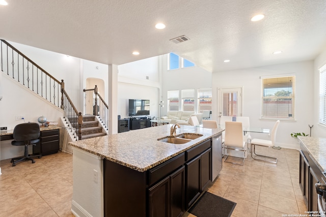 kitchen featuring dark brown cabinetry, a textured ceiling, sink, a kitchen island with sink, and a high ceiling