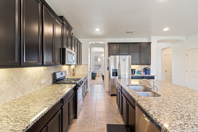 kitchen with tasteful backsplash, light stone counters, stainless steel appliances, light tile patterned floors, and sink