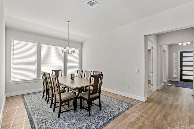 dining room with hardwood / wood-style flooring, a chandelier, a textured ceiling, and vaulted ceiling