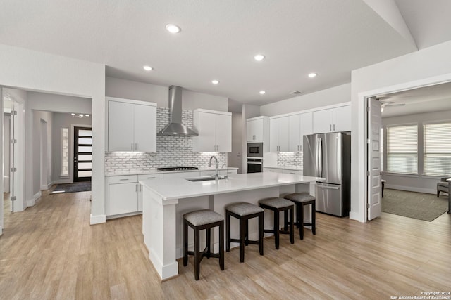 kitchen with white cabinetry, sink, appliances with stainless steel finishes, wall chimney exhaust hood, and an island with sink