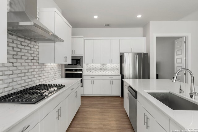 kitchen with stainless steel appliances, wall chimney range hood, white cabinets, and sink