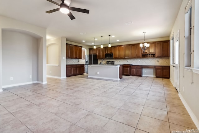 kitchen featuring black fridge, decorative light fixtures, decorative backsplash, sink, and a kitchen island with sink