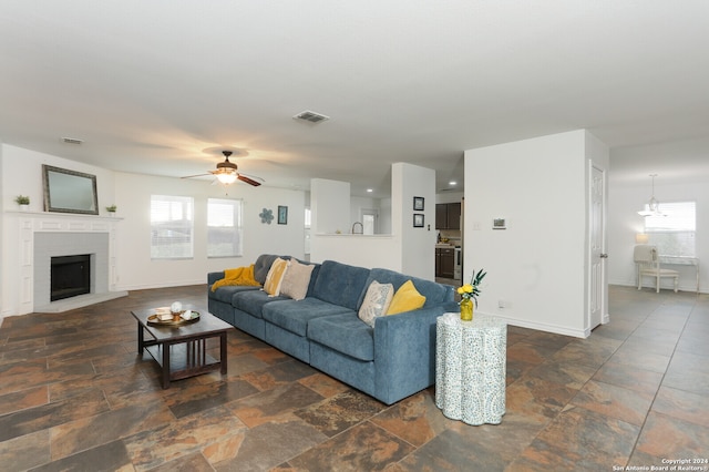 living room with a brick fireplace, plenty of natural light, and ceiling fan