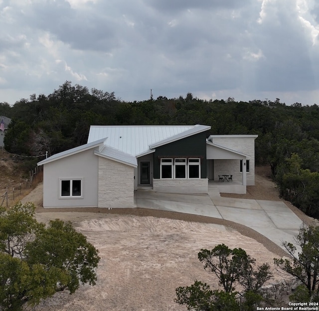 2920 Rocky Ridge Loop, Canyon Lake, TX 78133 - mid-century modern home featuring stone siding, a patio area, metal roof, and a forest view
