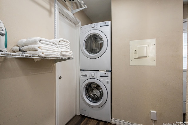 clothes washing area with dark hardwood / wood-style flooring, stacked washer and clothes dryer, and electric panel