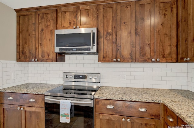 kitchen with backsplash, appliances with stainless steel finishes, and light stone countertops