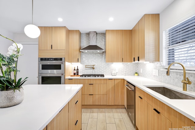 kitchen with sink, wall chimney range hood, backsplash, appliances with stainless steel finishes, and light brown cabinetry