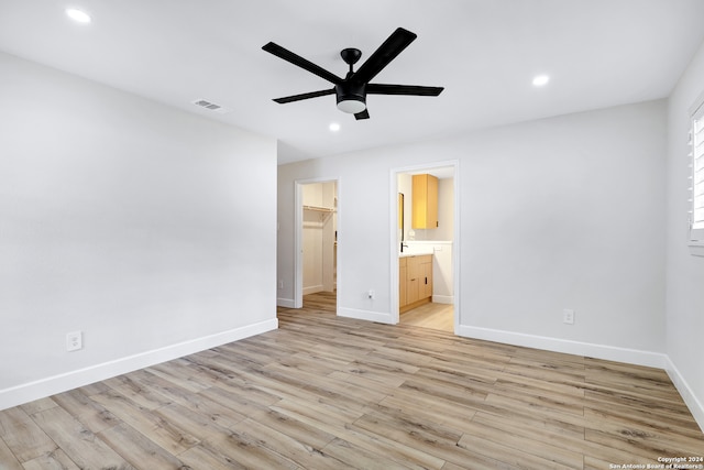 unfurnished bedroom featuring ensuite bathroom, ceiling fan, a spacious closet, a closet, and light wood-type flooring