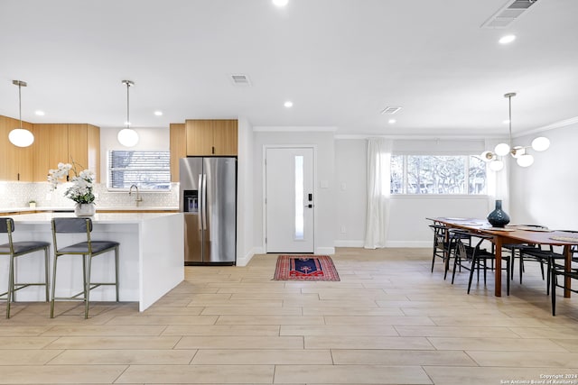 kitchen featuring stainless steel refrigerator with ice dispenser, a kitchen bar, backsplash, decorative light fixtures, and crown molding