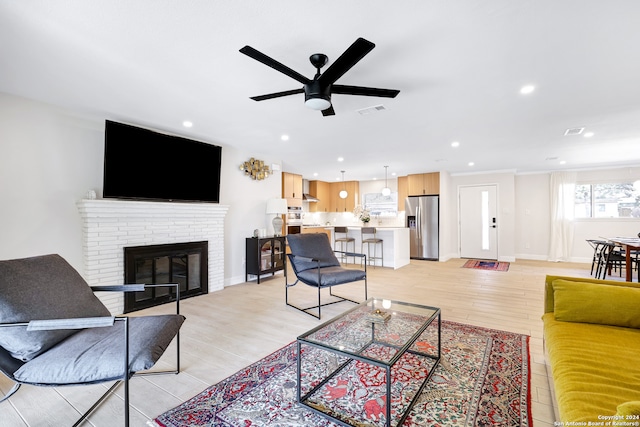 living room featuring a brick fireplace, light hardwood / wood-style floors, and ceiling fan