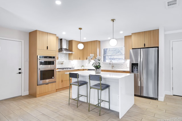 kitchen featuring appliances with stainless steel finishes, decorative light fixtures, a center island, and wall chimney range hood