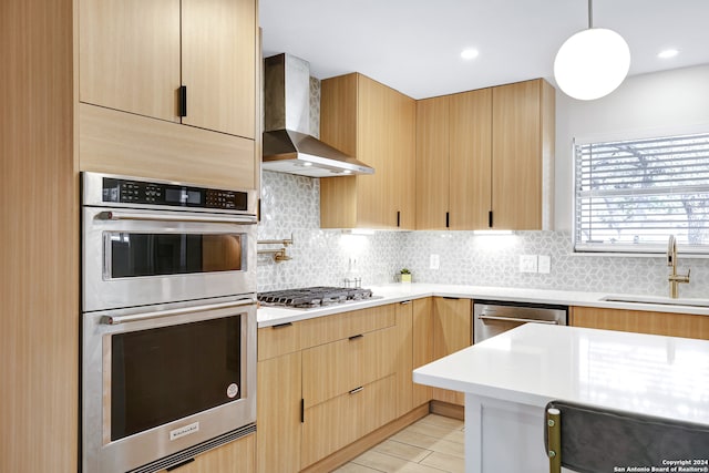 kitchen featuring wall chimney range hood, sink, decorative backsplash, and appliances with stainless steel finishes