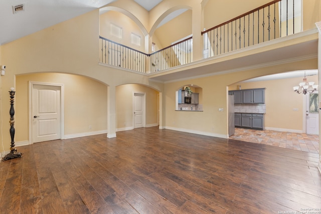 unfurnished living room with a towering ceiling, dark hardwood / wood-style floors, and an inviting chandelier