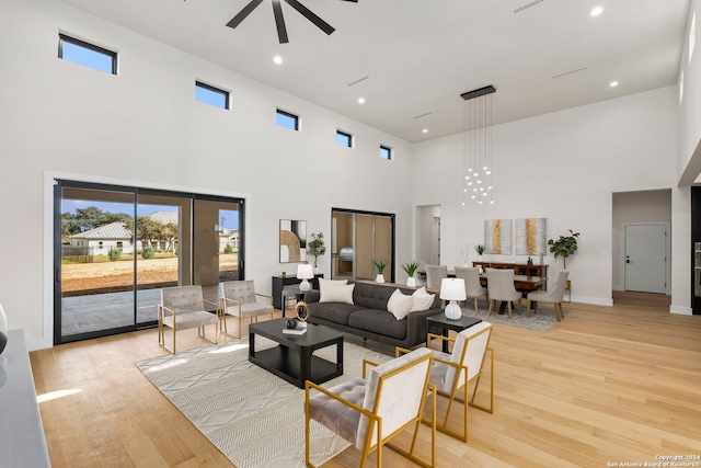 living room with ceiling fan, a towering ceiling, and light wood-type flooring