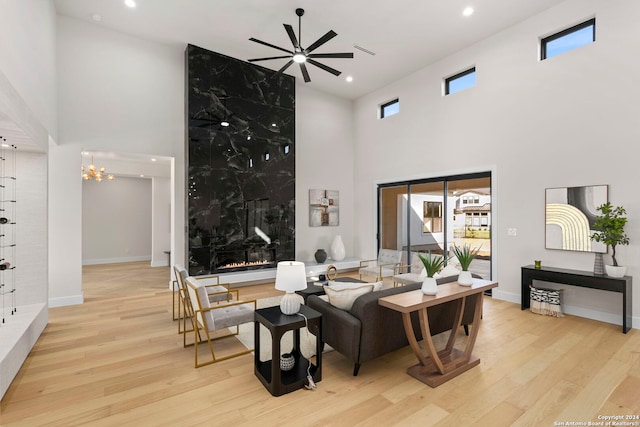 living room with ceiling fan with notable chandelier, light hardwood / wood-style floors, and a towering ceiling