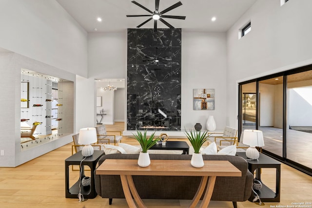 living room with ceiling fan with notable chandelier, a high ceiling, and light hardwood / wood-style flooring