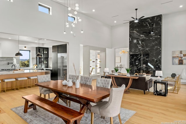 dining room featuring ceiling fan, light wood-type flooring, sink, and a towering ceiling