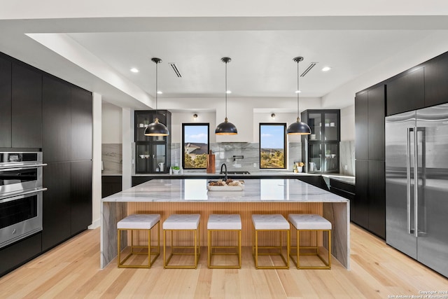 kitchen with a large island, light hardwood / wood-style flooring, pendant lighting, and appliances with stainless steel finishes