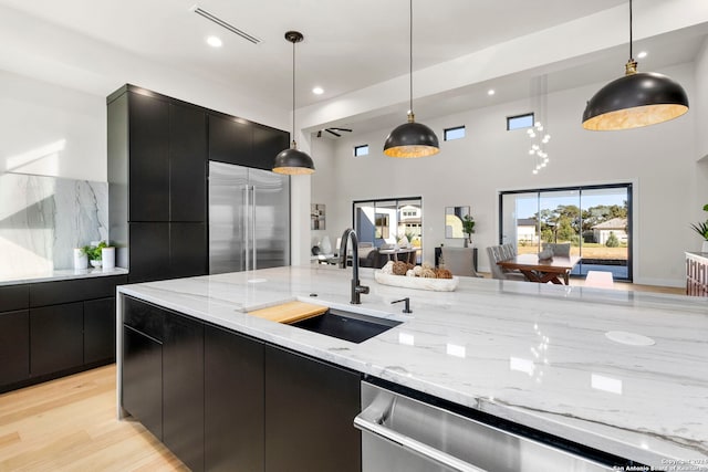 kitchen featuring light wood-type flooring, stainless steel appliances, sink, decorative light fixtures, and a high ceiling