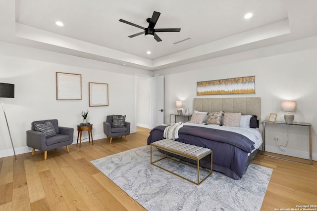 bedroom with hardwood / wood-style flooring, ceiling fan, and a tray ceiling