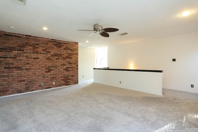 carpeted empty room featuring ceiling fan, brick wall, and a textured ceiling