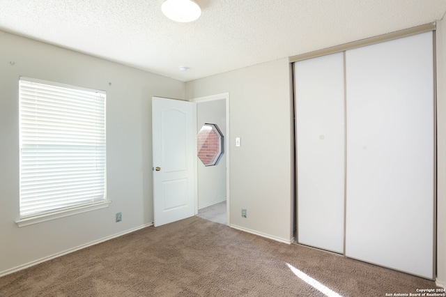 unfurnished bedroom featuring carpet, a textured ceiling, a closet, and multiple windows