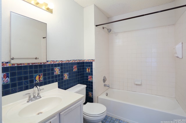 full bathroom with tiled shower / bath combo, a textured ceiling, toilet, vanity, and tile walls