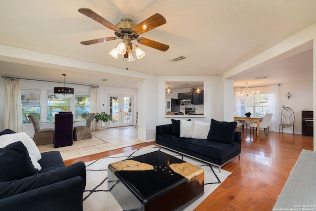 living room with ceiling fan with notable chandelier, french doors, a textured ceiling, and light hardwood / wood-style flooring