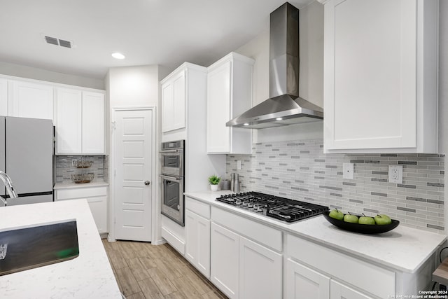 kitchen featuring appliances with stainless steel finishes, light stone countertops, light hardwood / wood-style floors, white cabinets, and wall chimney exhaust hood