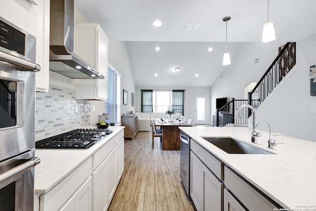 kitchen with appliances with stainless steel finishes, sink, vaulted ceiling, wall chimney exhaust hood, and light hardwood / wood-style flooring