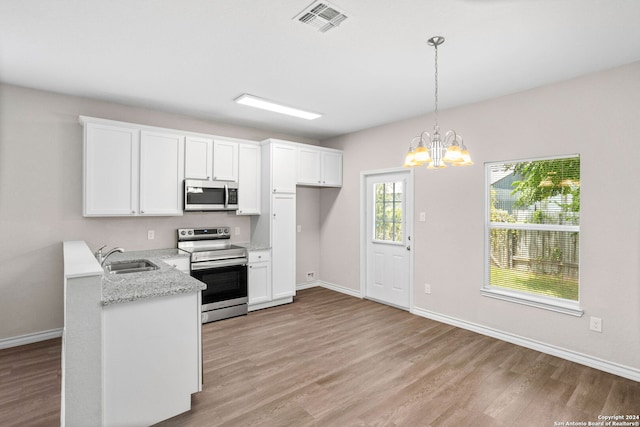 kitchen with appliances with stainless steel finishes, decorative light fixtures, sink, white cabinets, and light hardwood / wood-style flooring