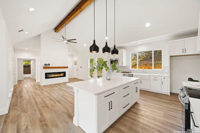 kitchen with white cabinets, light hardwood / wood-style floors, beamed ceiling, and appliances with stainless steel finishes