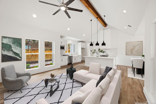 living room featuring ceiling fan, sink, light hardwood / wood-style flooring, beamed ceiling, and high vaulted ceiling