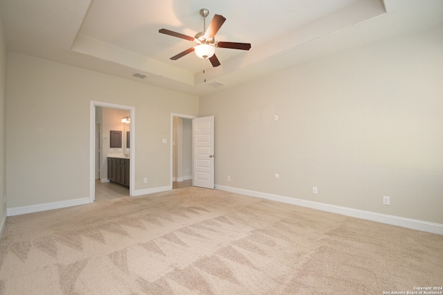 unfurnished bedroom featuring ceiling fan, connected bathroom, a raised ceiling, and light colored carpet