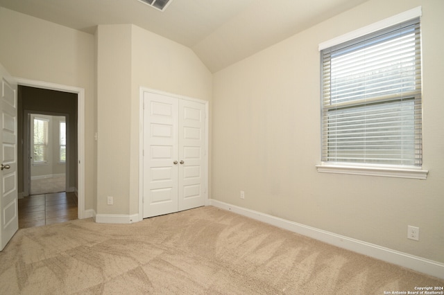 unfurnished bedroom featuring a closet, multiple windows, lofted ceiling, and light carpet