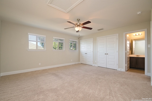 unfurnished bedroom with ensuite bathroom, light colored carpet, ceiling fan, and two closets